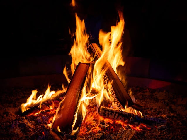 Campfire burning beside a still lake at dusk, representing transformation and inner light